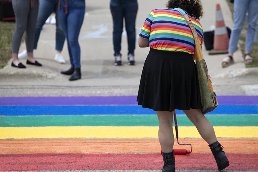 A person wearing a rainbow shirt helps to paint the road in rainbow shades.